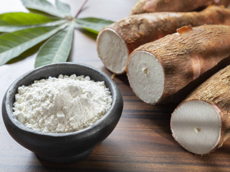 Bol de farine de manioc blanche avec racines de manioc coupées sur table en bois