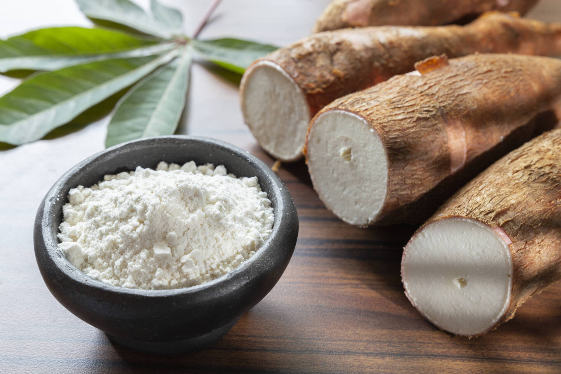 Bol de farine de manioc blanche avec racines de manioc coupées sur table en bois