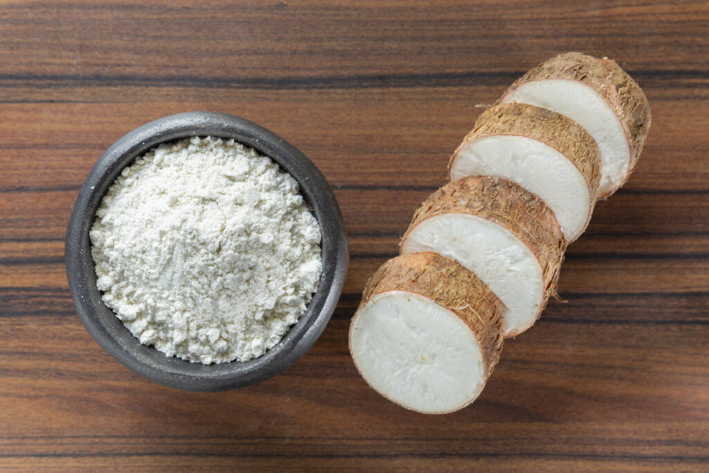 Bol de farine de manioc vue du dessus avec racine de manioc tranchée sur planche en bois